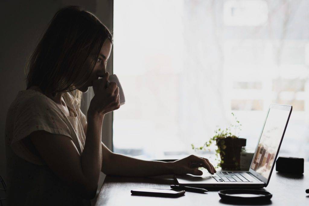woman drinking coffee working on a laptop